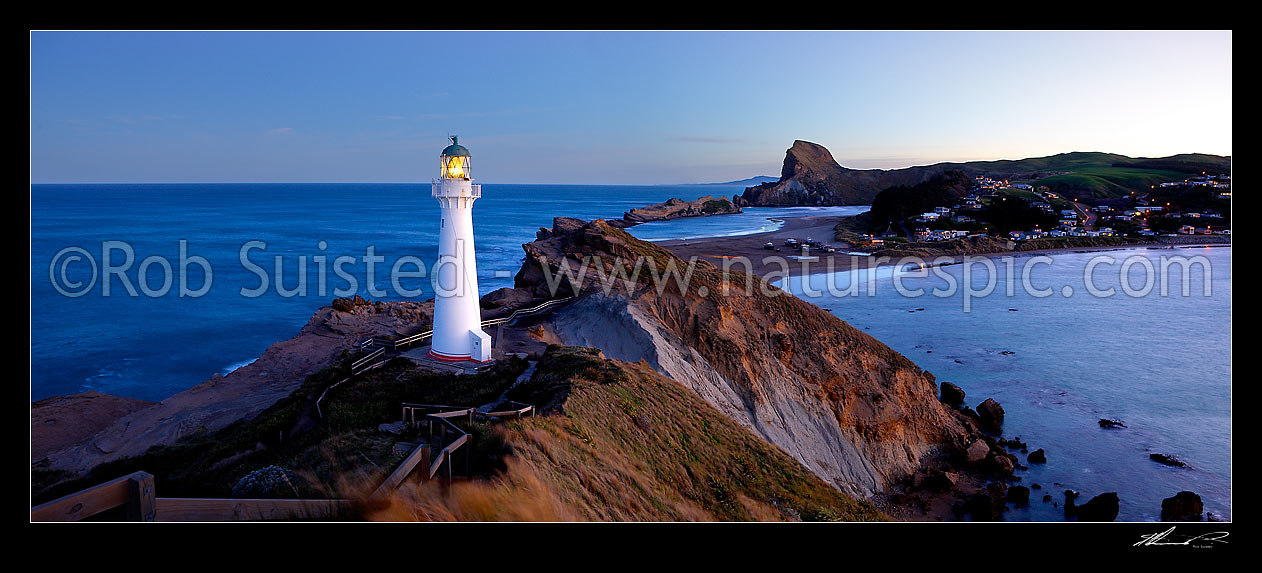 Image of Castlepoint Lighthouse (1913) at dusk, looking across reef, sandbar and lagoon towards Castle rock (162m). Township and beach at right. Castlepoint scenic reserve. Panorama, Castlepoint, Masterton District, Wellington Region, New Zealand (NZ) stock photo image