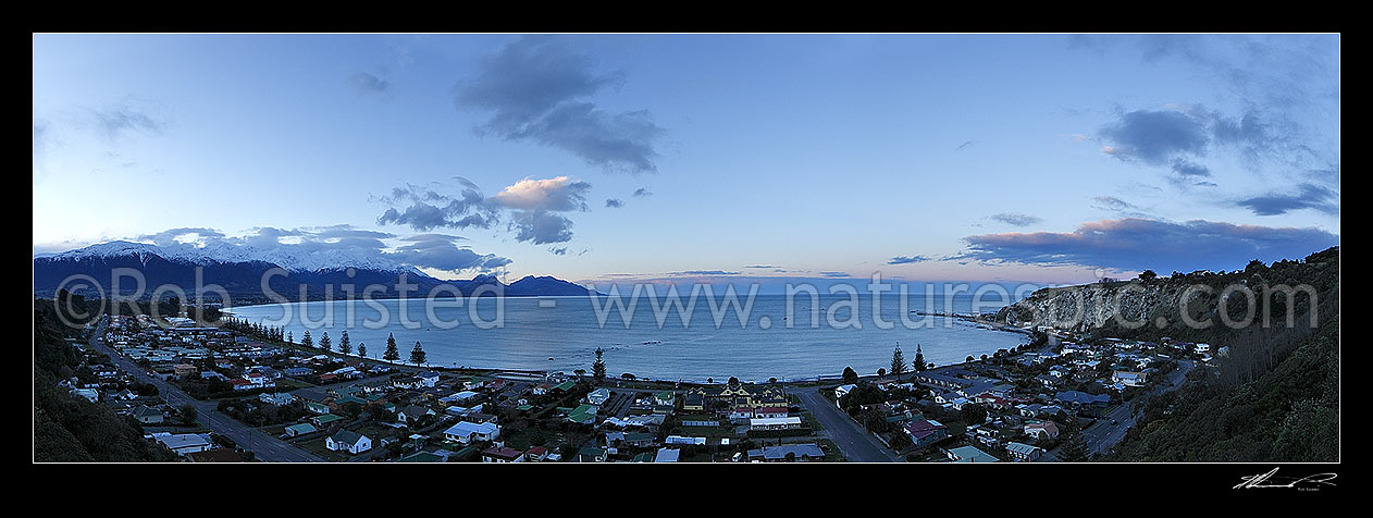 Image of Kaikoura township and bay at dusk in winter with snow on the Seaward Kaikoura Ranges at left. Panorama, Kaikoura, Kaikoura District, Canterbury Region, New Zealand (NZ) stock photo image