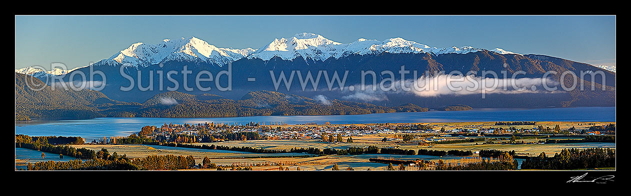 Image of Lake Te Anau and Te Anau township, with winter snow capped Murchison Mountains and Fiordland National Park beyond. Early morning panorama, Te Anau, Southland District, Southland Region, New Zealand (NZ) stock photo image