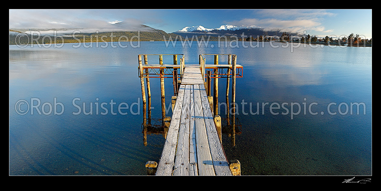 Image of Lake Te Anau and lakeside jetty, with winter snow capped Murchison Mountains and Fiordland National Park beyond. Calm early morning panorama, Te Anau, Southland District, Southland Region, New Zealand (NZ) stock photo image