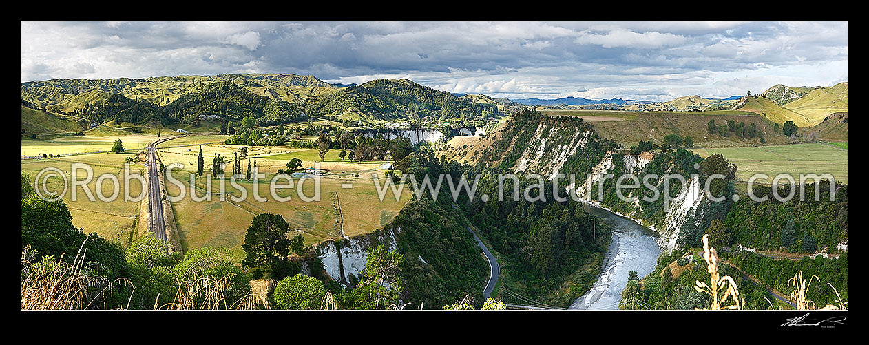 Image of Mangaweka township visible beyond farmland and white siltstone cliffs above the Rangitikei River. North Island main trunk line left. Panorama, Mangaweka, Rangitikei District, Manawatu-Wanganui Region, New Zealand (NZ) stock photo image