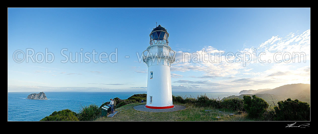 Image of East Cape Lighthouse panorama at dusk with tourist visitors taking photograph. East Island (Whangoakeno) at left, East Cape, Gisborne District, Gisborne Region, New Zealand (NZ) stock photo image