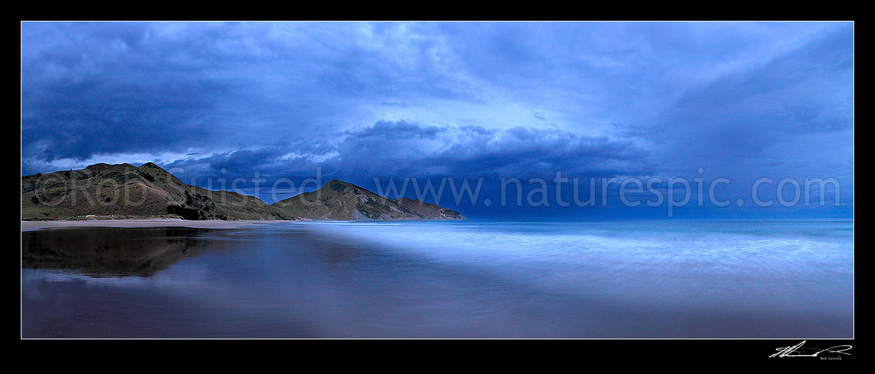 Image of Kaiaua Bay Beach moody twilight panorama, as storm clouds gather, with Marau Point left. Waves breaking on beach blurred in movement, Tolaga Bay, Gisborne District, Gisborne Region, New Zealand (NZ) stock photo image