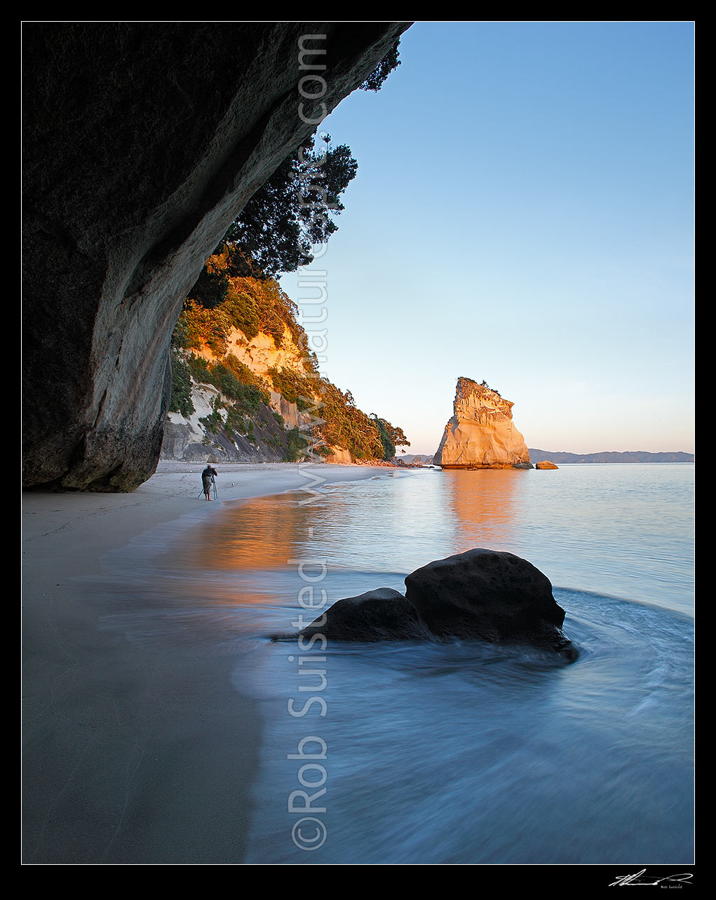 Image of Cathedral Cove peaceful sunrise morning, looking through rock tunnel or cave. Coromandel Peninsula. Photographer photographing the dawn, Hahei, Coromandel Peninsula, Thames-Coromandel District, Waikato Region, New Zealand (NZ) stock photo image