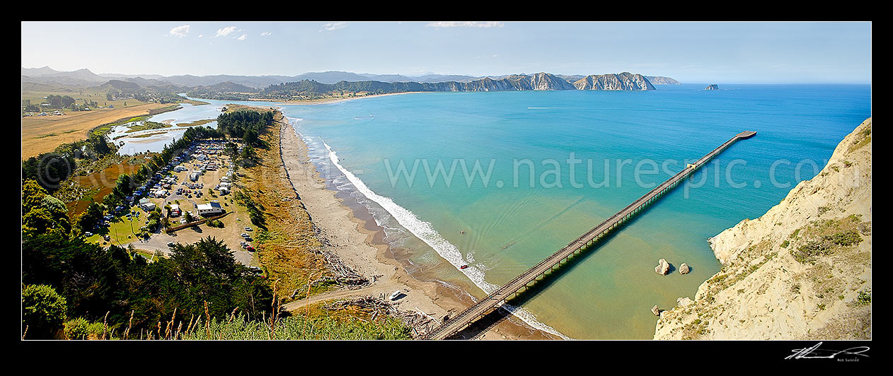 Image of Tolaga Bay wharf in Tolaga Bay. Uawa River mouth and town top left. NZ's longest wharf at 660 metres. Mt Hikurangi distant centre. Panorama, Tolaga Bay, East Coast, Gisborne District, Gisborne Region, New Zealand (NZ) stock photo image