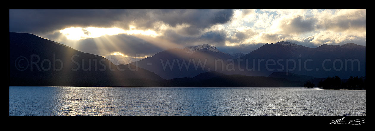 Image of Lake Te Anau and Fiordland with sun rays breaking through cloud near Brod Bay. Murchison Mountains centre and Bluegum Point right. Panorama, Fiordland National Park, Southland District, Southland Region, New Zealand (NZ) stock photo image