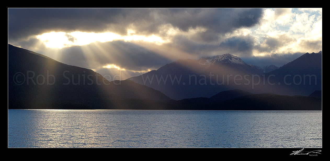 Image of Lake Te Anau and Fiordland with sun rays breaking through cloud near Brod Bay. Murchison Mountains centre. Panorama, Fiordland National Park, Southland District, Southland Region, New Zealand (NZ) stock photo image