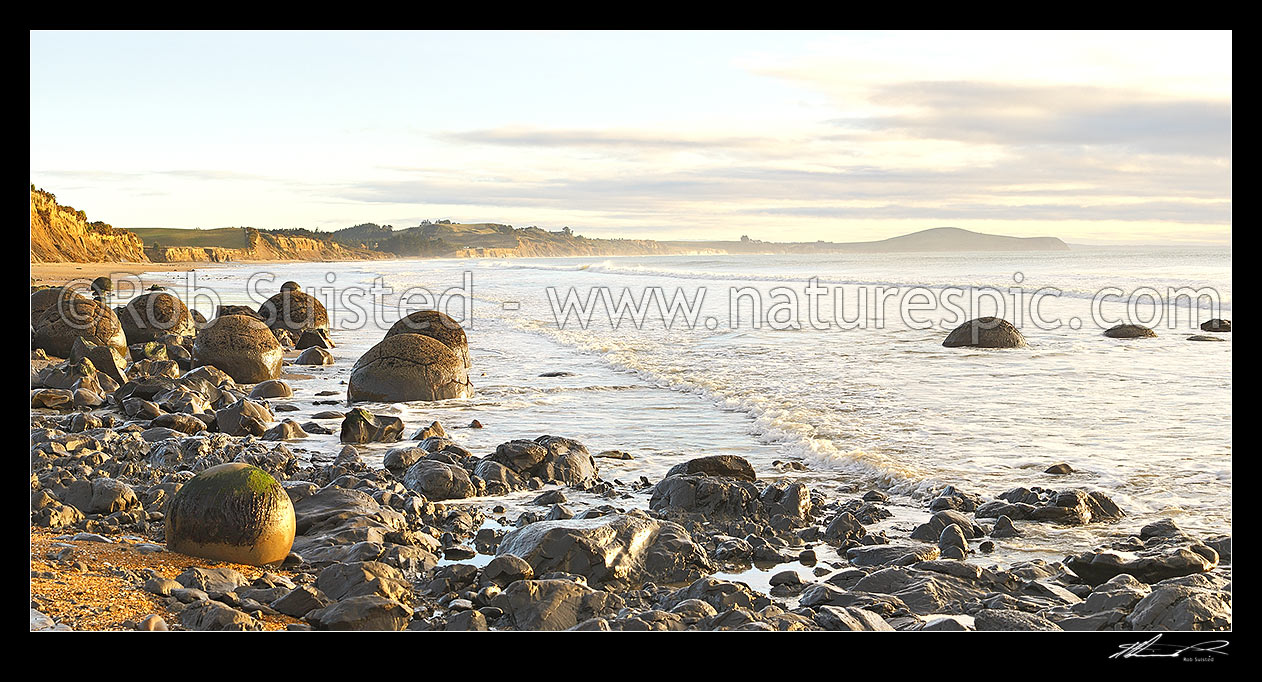 Image of Moeraki Boulders / Kaihinaki, 60 Million year old mudstone concretions at sunrise with Lookout Bluff distant right. Panorama, Moeraki, Waitaki District, Canterbury Region, New Zealand (NZ) stock photo image