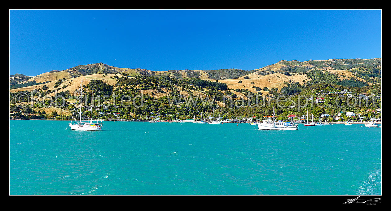 Image of Akaroa township panorama taken from the sea with sailboats and fishing boats moored in French Bay, Banks Peninsula, Christchurch City District, Canterbury Region, New Zealand (NZ) stock photo image