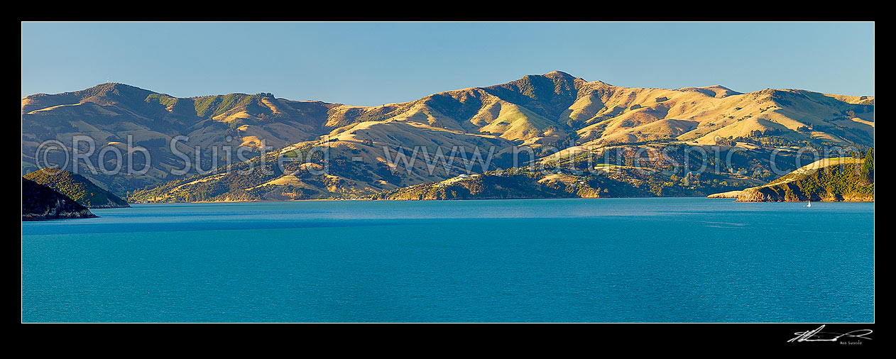 Image of Akaroa upper harbour with Mt Pearce and Duvauchelle at left, Duvauchelle Peak (738m) and Robinsons Bay centre, and Takamatua with passing sailboat (right) from near Wainui. Banks Peninsula. Panorama, Akaroa, Christchurch City District, Canterbury Region, New Zealand (NZ) stock photo image