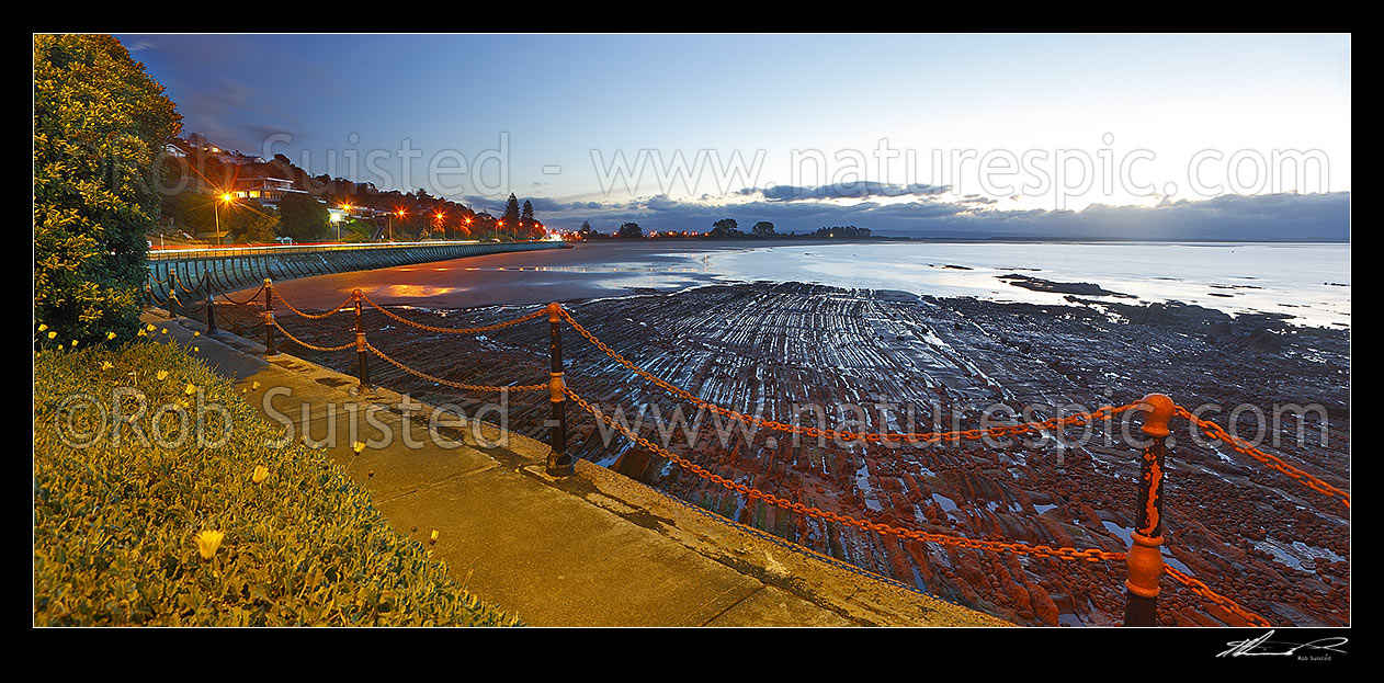 Image of Tahunanui Beach evening sunset panorama with dramatic geologial rock patterns in foreground, and Rocks Road, Moana, left, Nelson, Nelson City District, Nelson Region, New Zealand (NZ) stock photo image