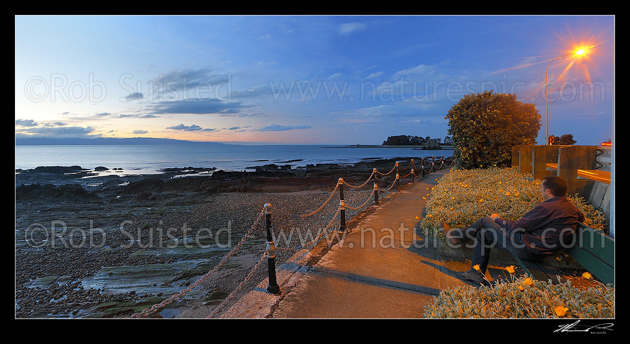 Image of Tahunanui Beach waterfront walkway along Rocks Road and Wakefield Quay, with person watching sunset over Tasman Bay. Panorama, Nelson, Nelson City District, Nelson Region, New Zealand (NZ) stock photo image