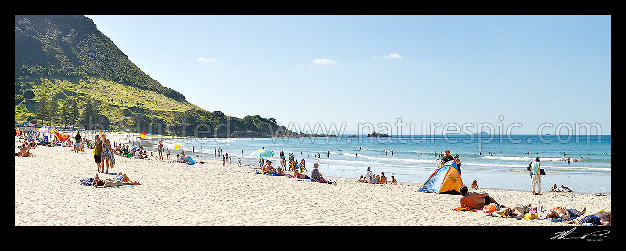 Image of Mount Maunganui beach panorama, with people sunbathing and swimming, and distant Karewa Island (right) beyond. The Mount peak at left, Mount Maunganui, Tauranga District, Bay of Plenty Region, New Zealand (NZ) stock photo image