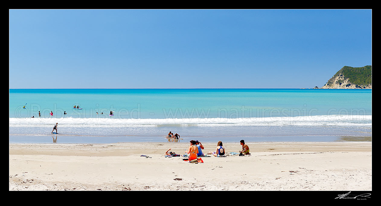 Image of Families enjoying the summer on Waipiro Bay beach with azure blue water. Swimming, digging, sunbathing, kayaking and wave skis in surf. Panorama, Waipiro Bay, East Coast, Gisborne District, Gisborne Region, New Zealand (NZ) stock photo image