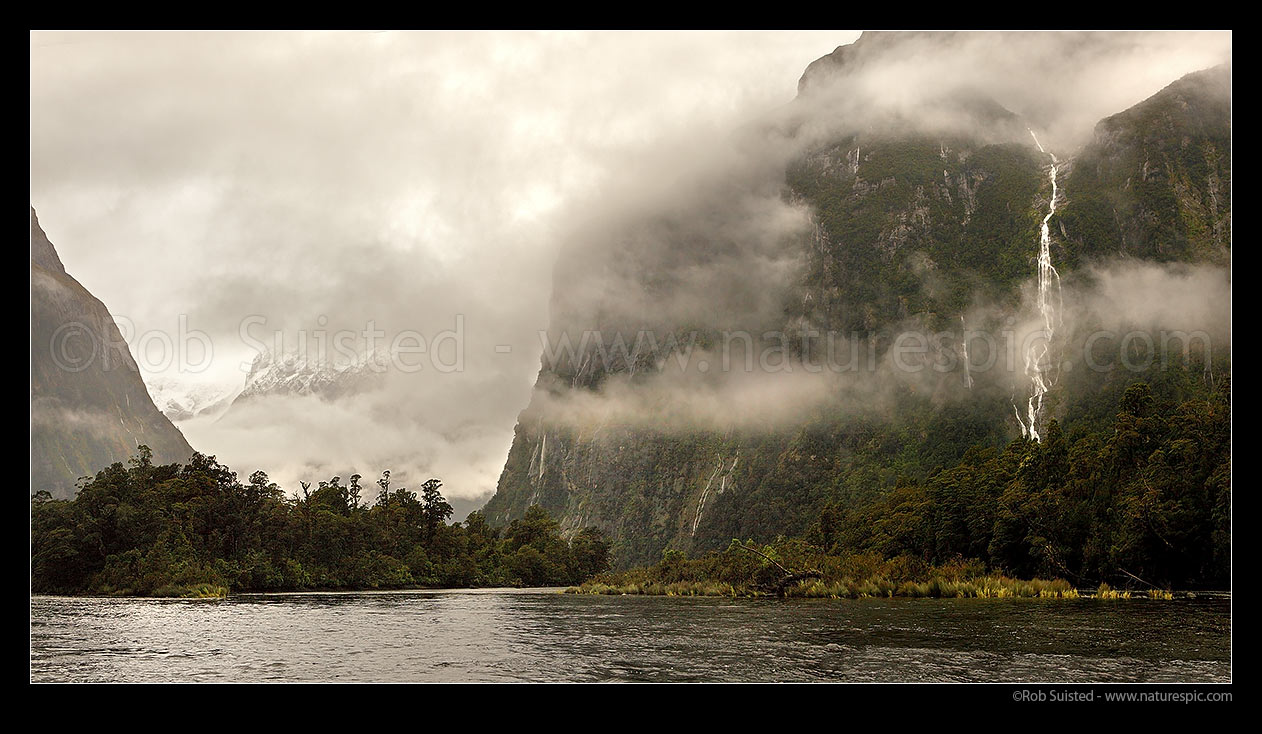 Image of Moody Milford Sound. Arthur River looking toward Darran Mountains & Cleddau Valley (left), and Sheerdown Hills (right) with fresh waterfalls from rain. Panorama, Milford Sound, Fiordland National Park, Southland District, Southland Region, New Zealand (NZ) stock photo image