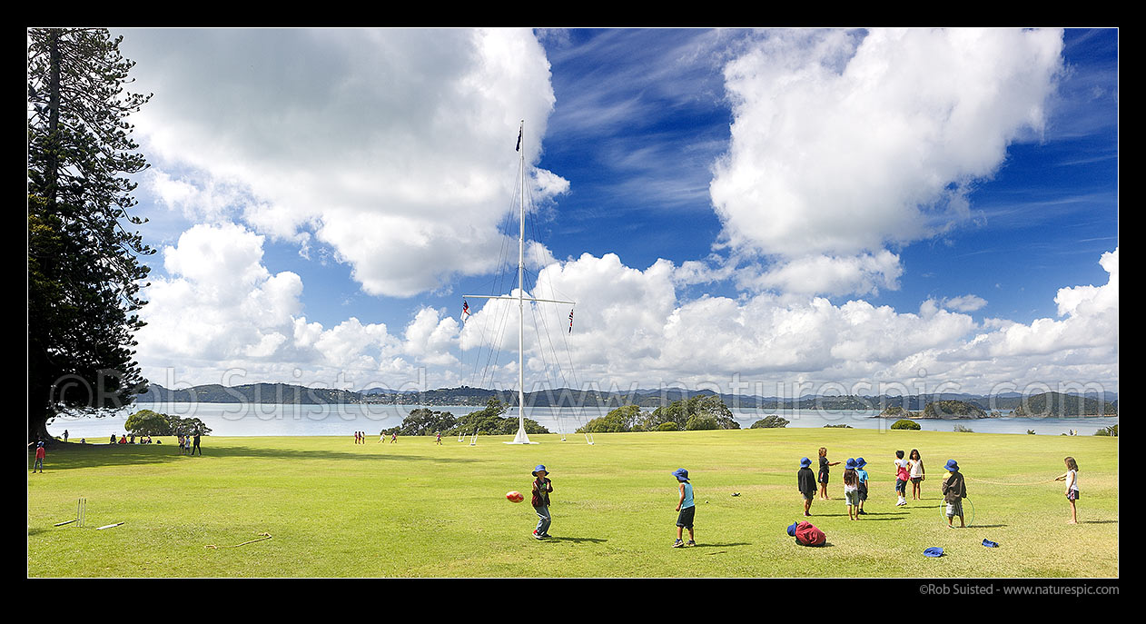 Image of Waitangi Treaty Grounds with visiting school children playing on grass. Naval flagstaff standing where Te Tiriti o Waitangi (Treaty of Waitangi) was signed. Panorama, Waitangi, Bay of Islands, Far North District, Northland Region, New Zealand (NZ) stock photo image