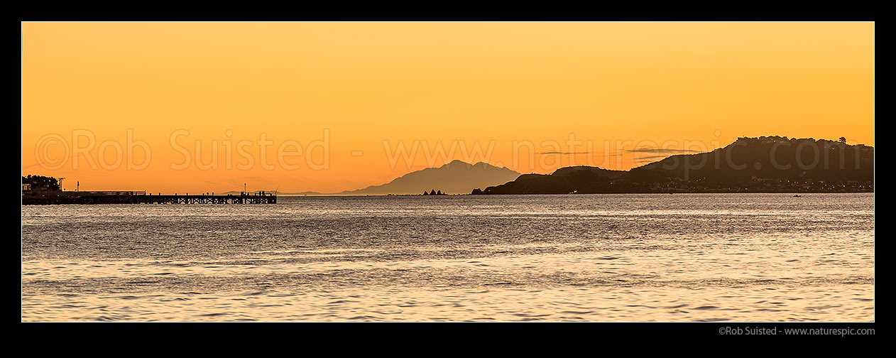 Image of Wellington Harbour entrance sunset. Eastbourne wharf with fishers and South Island Seaward Kaikoura Ranges in distance. Seatoun and Point Dorset at right. Panorama, Eastbourne, Hutt City District, Wellington Region, New Zealand (NZ) stock photo image