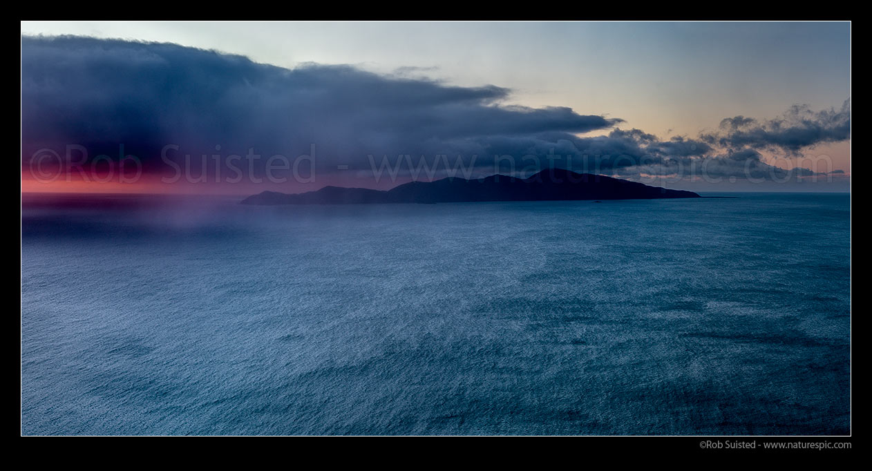 Image of Kapiti Island with sleety rain showers moving in from Cook Strait on a moody sunset. Rauoterangi Chanel (Otaheke Strait) at right. Panorama, Paekakariki, Kapiti Coast District, Wellington Region, New Zealand (NZ) stock photo image