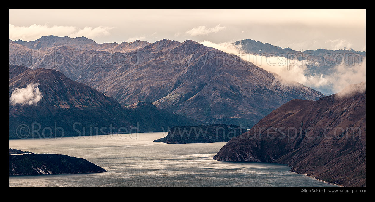 Image of Lake Wanaka moody mountains. Mou Whao Island centre with Twin Peaks and Minaret Burn Station above. Mt Albert (2064m)distant centre right. The Peninsula at right, Mou Tapu island bottom left. Panorama, Wanaka, Queenstown Lakes District, Otago Region, New Zealand (NZ) stock photo image