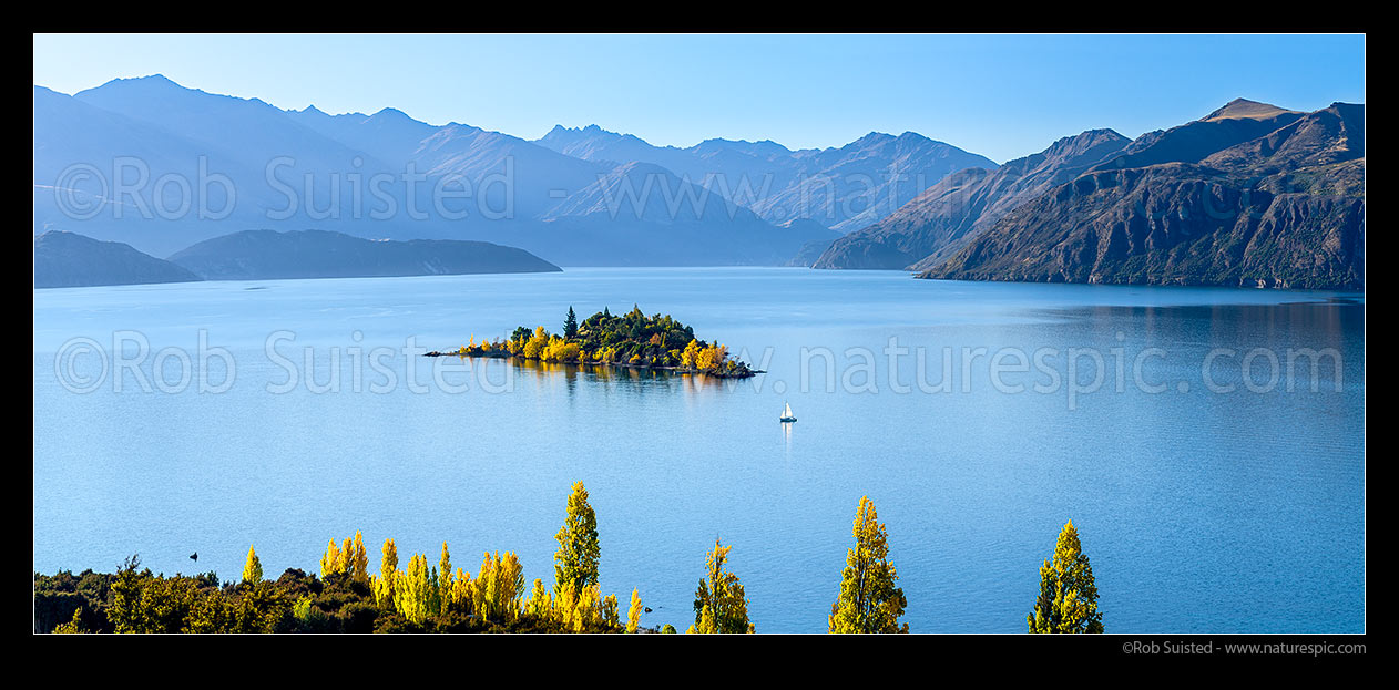 Image of Lake Wanaka panorama with sailboat passing Ruby Island in autumn colours, Wanaka, Queenstown Lakes District, Otago Region, New Zealand (NZ) stock photo image