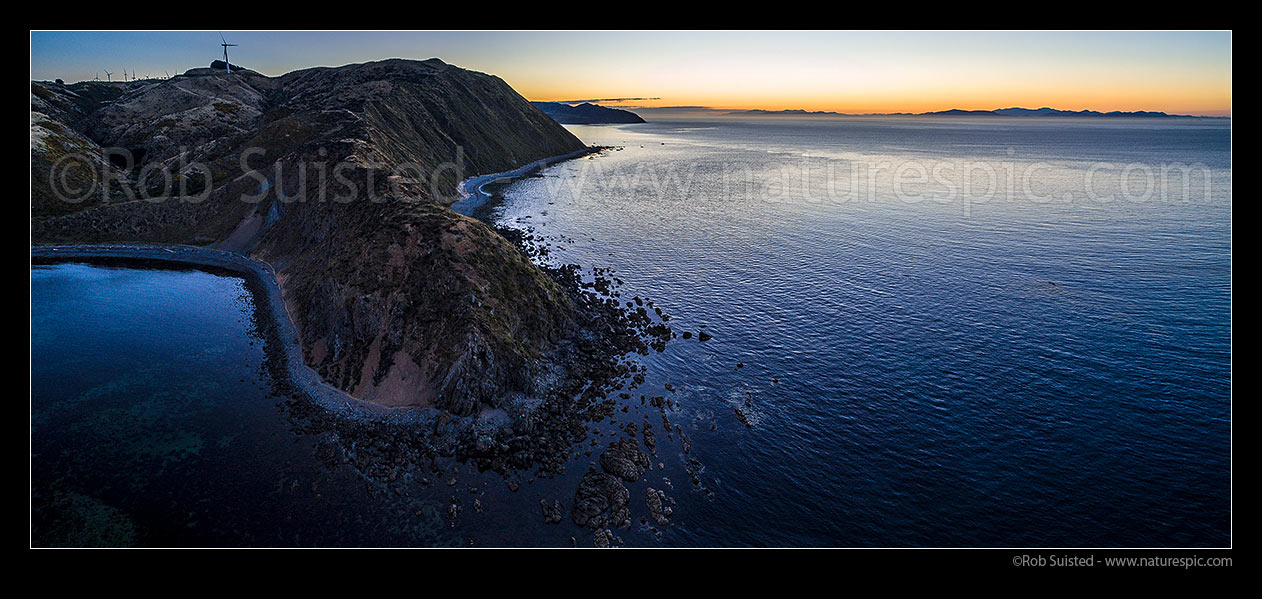 Image of Makara Beach sunset over Cook Strait. Wharehou Bay far left, Ohau Point centre, and South Island at right. West Wind Farm turbines above left. Aerial panorama, Makara Beach, Wellington City District, Wellington Region, New Zealand (NZ) stock photo image