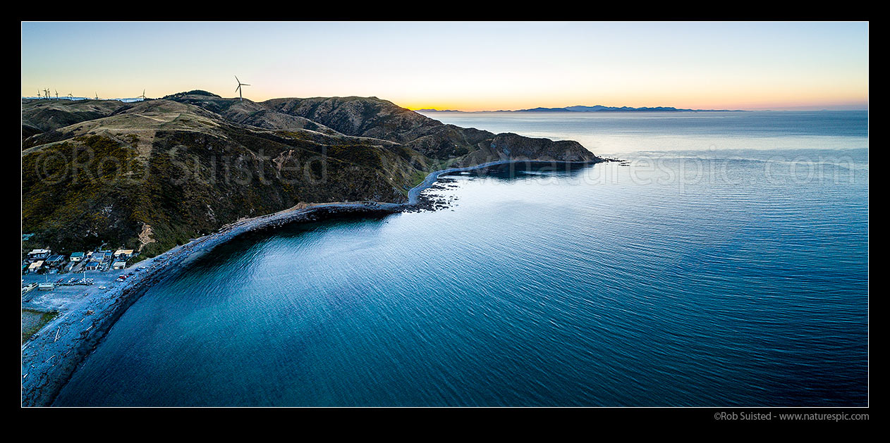 Image of Makara Beach sunset. Ohariu Bay and Makara village at left, Wharehou Bay centre and South Island beyond over Cook Strait. West Wind Farm turbines above. Aerial panorama, Makara Beach, Wellington City District, Wellington Region, New Zealand (NZ) stock photo image