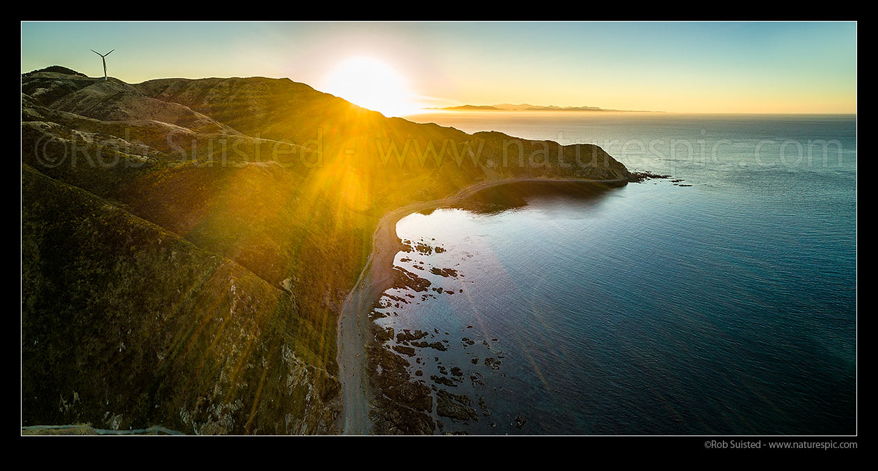 Image of Makara sunset over Wharehou Bay. South Island in distance, over Cook Strait. West Wind Farm turbine at left. Aerial panorama, Makara Beach, Wellington City District, Wellington Region, New Zealand (NZ) stock photo image