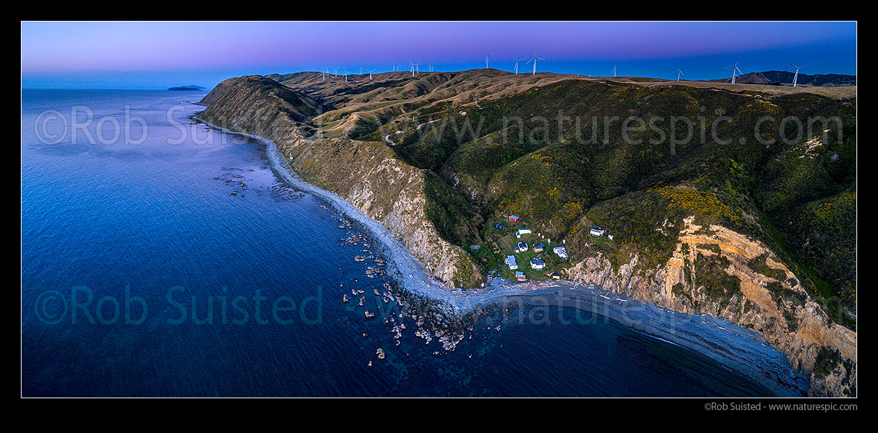 Image of Mill Creek Wind Farm turbines above Smiths Bay and baches on the Makara Beach coastline. Looking north towards Mana and Kapiti islands in the sunset after glow. Aerial panorama, Makara Beach, Wellington City District, Wellington Region, New Zealand (NZ) stock photo image