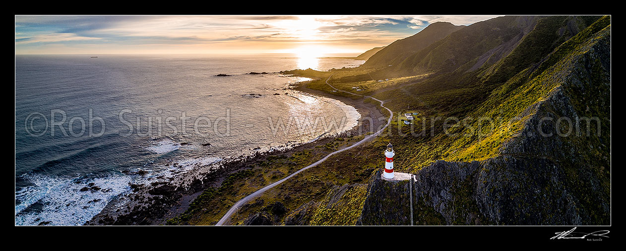 Image of Cape Palliser lighthouse above Palliser Bay baches and Kirikiri Bay on a moody sunset (Matakitakiakupe). Aerial panorama with golden evening sunset, Cape Palliser, South Wairarapa District, Wellington Region, New Zealand (NZ) stock photo image