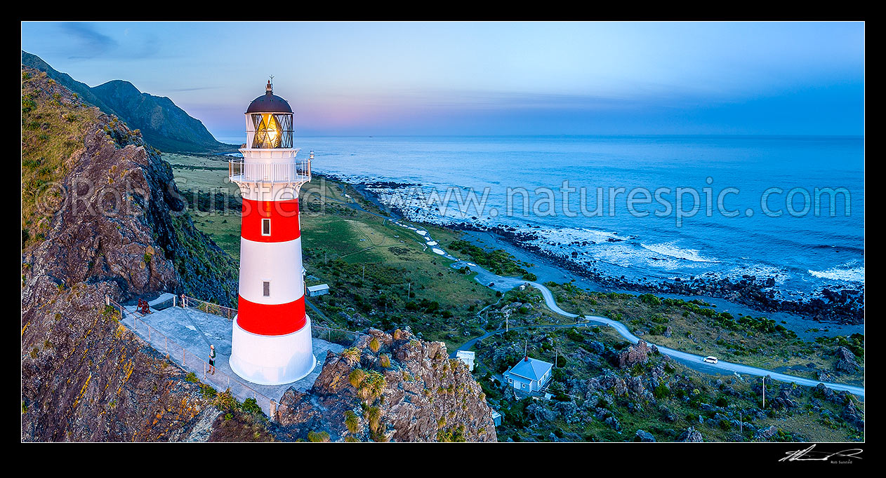 Image of Cape Palliser lighthouse on the southern most point of the North Island (Matakitakiakupe). Aerial panorama at dusk with Aoraki Ranges (Haurangi Forest Park) beyond, Cape Palliser, South Wairarapa District, Wellington Region, New Zealand (NZ) stock photo image