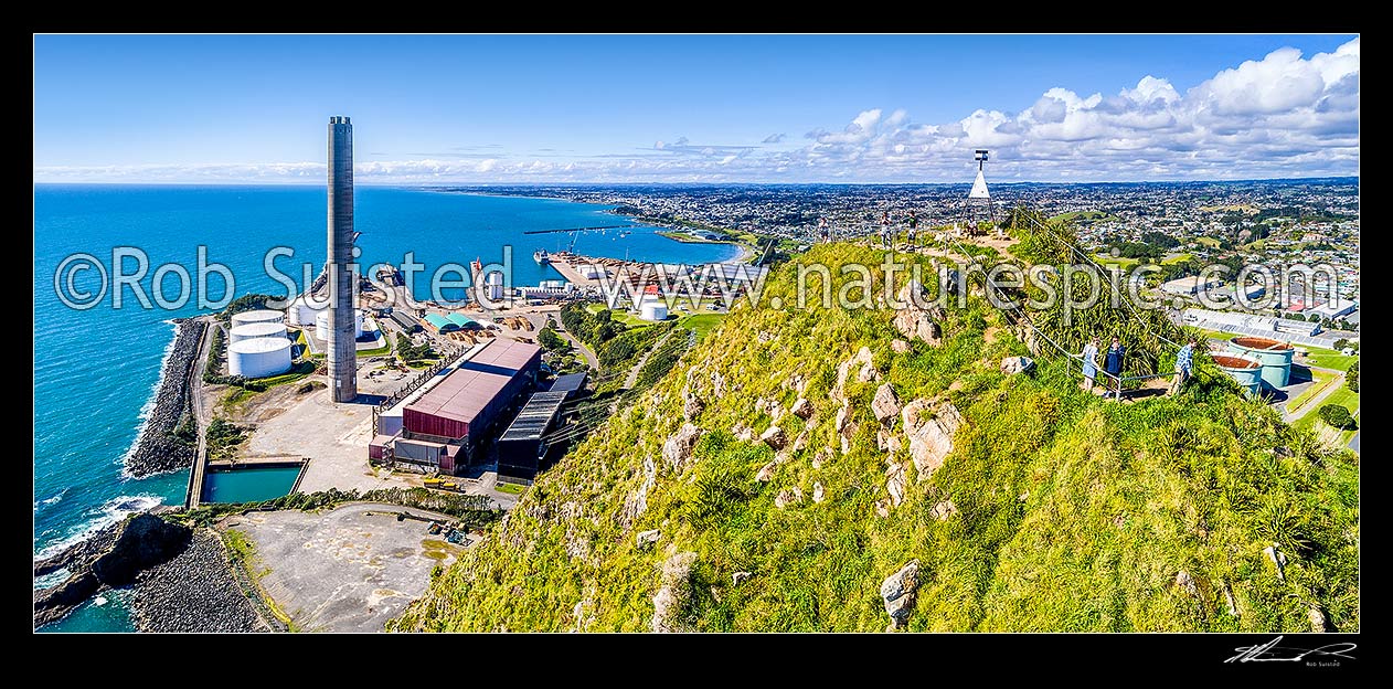 Image of Paritutu Rock summit trig and lookout with visitors (154m), with New Plymouth city and the New Plymouth power station and chimney (198m high) beyond. Aerial panorama, New Plymouth, New Plymouth District, Taranaki Region, New Zealand (NZ) stock photo image