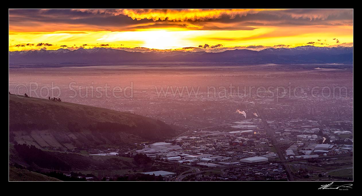 Image of Christchurch City and Canterbury plains on a calm winter evening with fog settling and snow on the Southern Alps beyond. Sunset panorama, Port Hills, Christchurch, Christchurch City District, Canterbury Region, New Zealand (NZ) stock photo image