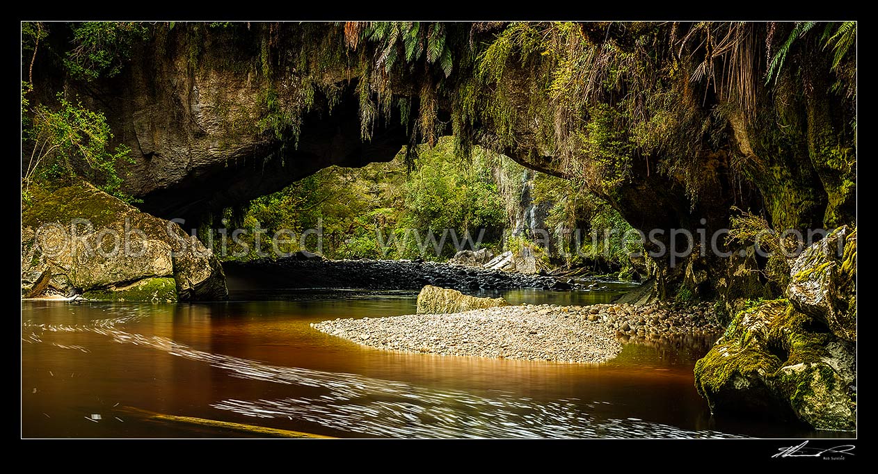 Image of Oparara Arch. The Oparara River entering the little Oparara arch (Moria Gate). Clean, dark vegetation and tanin stained water moving slowly under the limestone arch. Panorama, Karamea,Kahurangi National Park, Buller District, West Coast Region, New Zealand (NZ) stock photo image