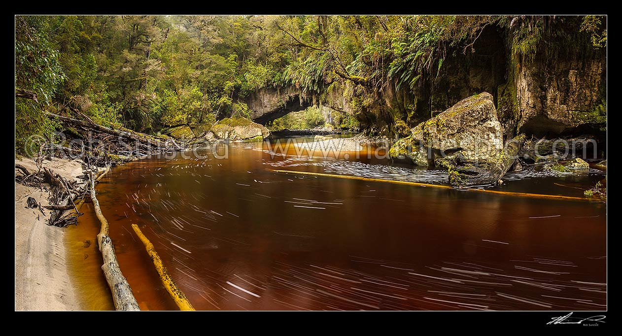 Image of Oparara River entering the little Oparara arch (Moria Gate). Clean, dark, tanin stained water moving slowly through the limestone arch. Panorama, Karamea,Kahurangi National Park, Buller District, West Coast Region, New Zealand (NZ) stock photo image