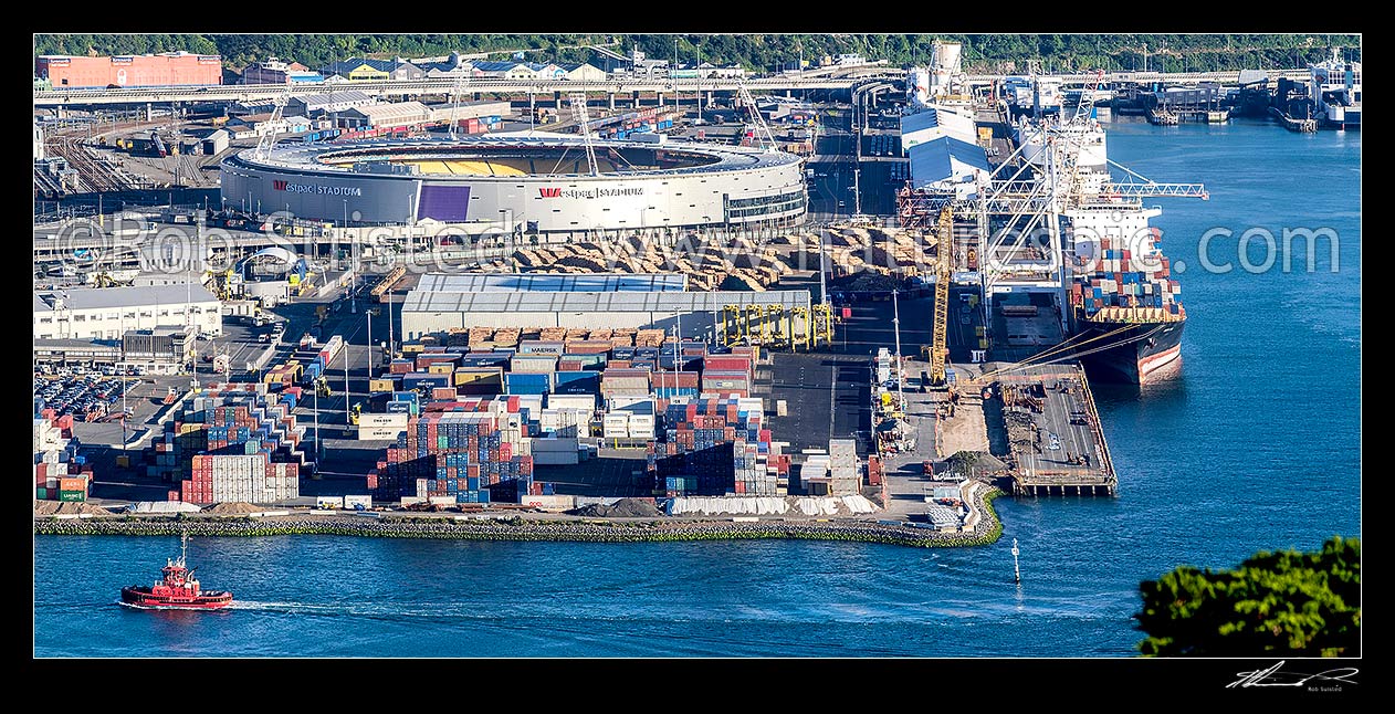 Image of Wellington Container Terminal, CentrePort, with ships loading alongside. Passing Tugboat Tapuhi, and Westpac Stadium beyond, Wellington, Wellington City District, Wellington Region, New Zealand (NZ) stock photo image