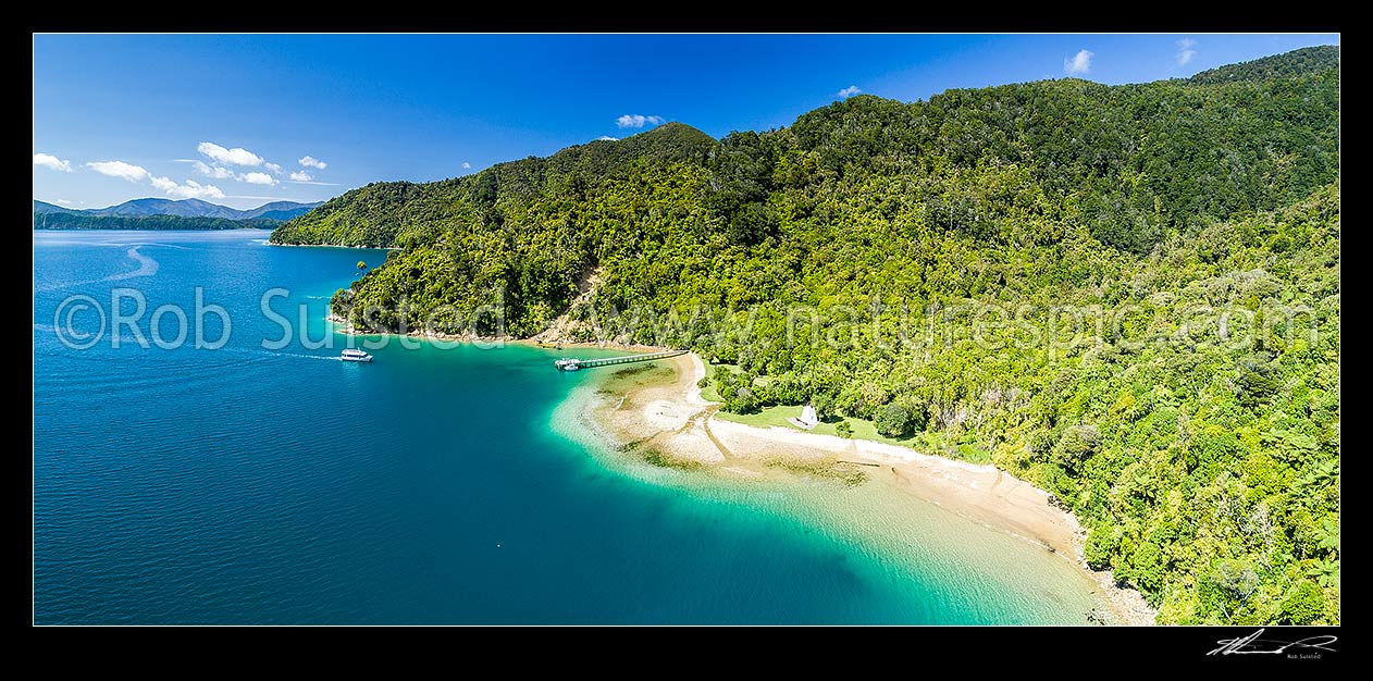 Image of Ship Cove (Meretoto) and Captain Cook's Monument in the outer Queen Charlotte Sound (Totaranui). Aerial panorama with people arriving to start the Queen Charlotte Walking Track, Marlborough Sounds, Marlborough District, Marlborough Region, New Zealand (NZ) stock photo image