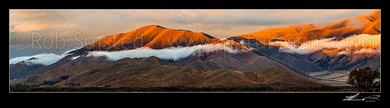 Image of MacKenzie Basin evening as sun sets over The Buscot Peak (1245m), with mist and cloud wisps. Benmore Range above. Panorama, Omarama, Waitaki District, Canterbury Region, New Zealand (NZ) stock photo image