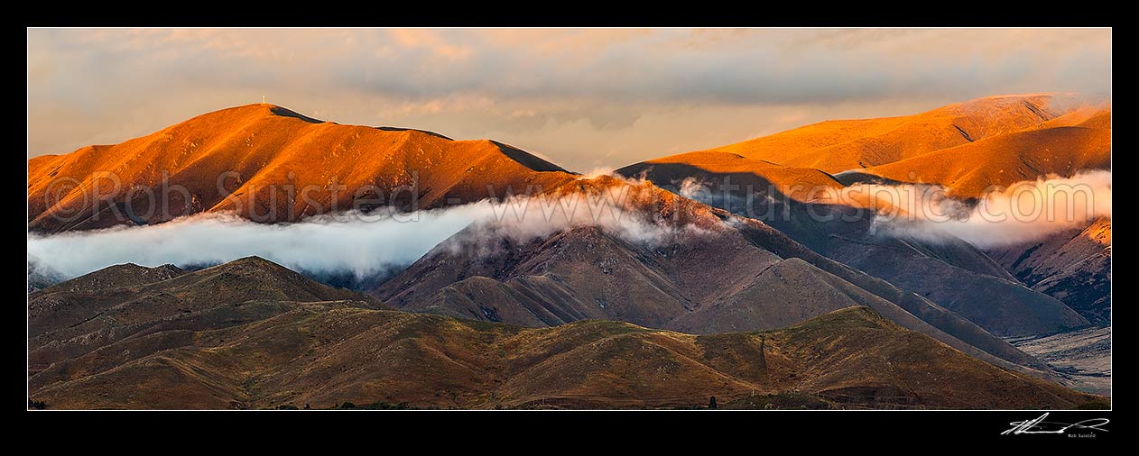 Image of MacKenzie Basin evening as sun sets over The Buscot Peak (left, 1245m), with mist and cloud wisps. Benmore Range and Benmore Peak far right. Panorama, Omarama, Waitaki District, Canterbury Region, New Zealand (NZ) stock photo image