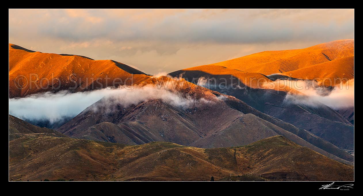 Image of MacKenzie Basin sunset over The Buscot and Benmore Peak and Benmore Range (right). Moody evening mist and wispy cloud hangs over ridges. Panorama, Omarama, Waitaki District, Canterbury Region, New Zealand (NZ) stock photo image