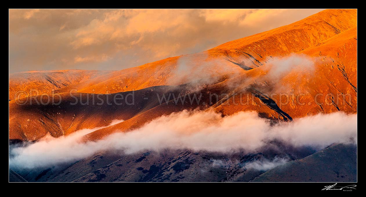 Image of Benmore Range high country sunset high above the MacKenzie Basin, with mist and evening cloud wisps strung over the ridges. Panorama, Omarama, Waitaki District, Canterbury Region, New Zealand (NZ) stock photo image