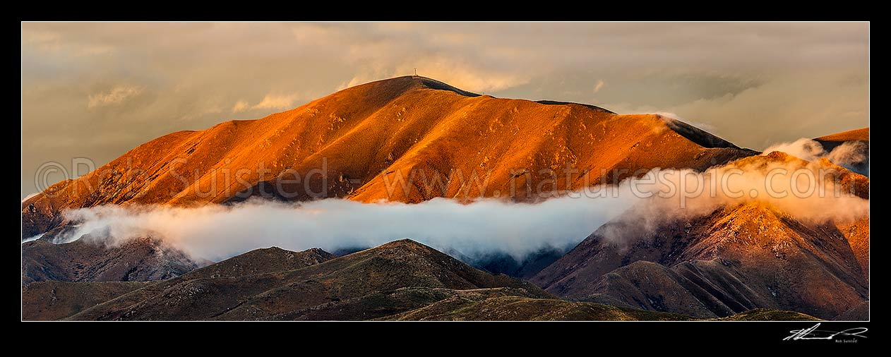 Image of The Buscot Peak (1245m) stands in evening sunlight above the MacKenzie Basin high country. Evening cloud cloaks the ridges. Panorama, Omarama, Waitaki District, Canterbury Region, New Zealand (NZ) stock photo image