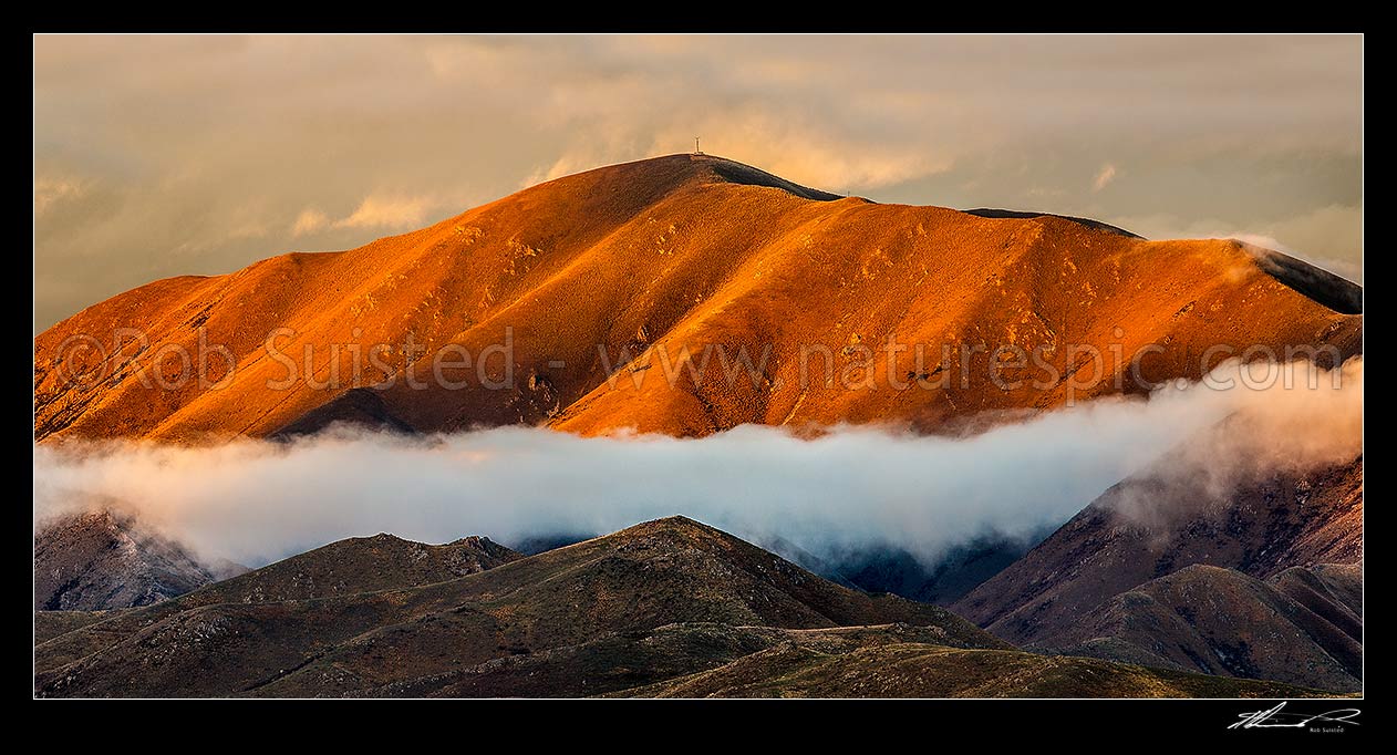 Image of The Buscot Peak (1245m) stands in evening sunlight above the MacKenzie Basin high country. Evening cloud cloaks the ridges. Panorama, Omarama, Waitaki District, Canterbury Region, New Zealand (NZ) stock photo image