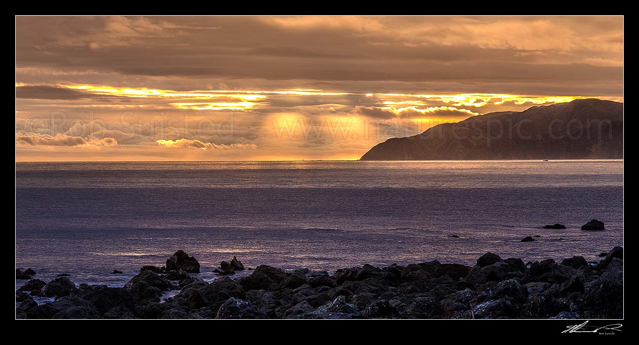 Image of Wellington South Coast and Cook Strait with spectactular light show at sunset over Sinclair Head (centre). Panorama, Turakirae Head, Hutt City District, Wellington Region, New Zealand (NZ) stock photo image