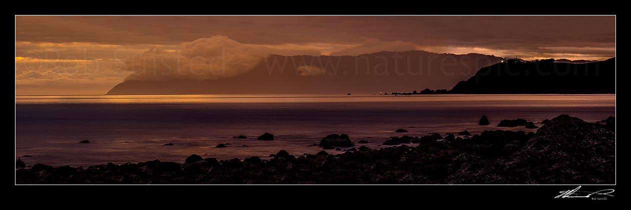 Image of Baring Head lighthouse (right) shining out over Cook Strait from Wellington harbour entrance at twilight. Sinclair Head on Wellington South Coast at left, Turakirae Head, Hutt City District, Wellington Region, New Zealand (NZ) stock photo image