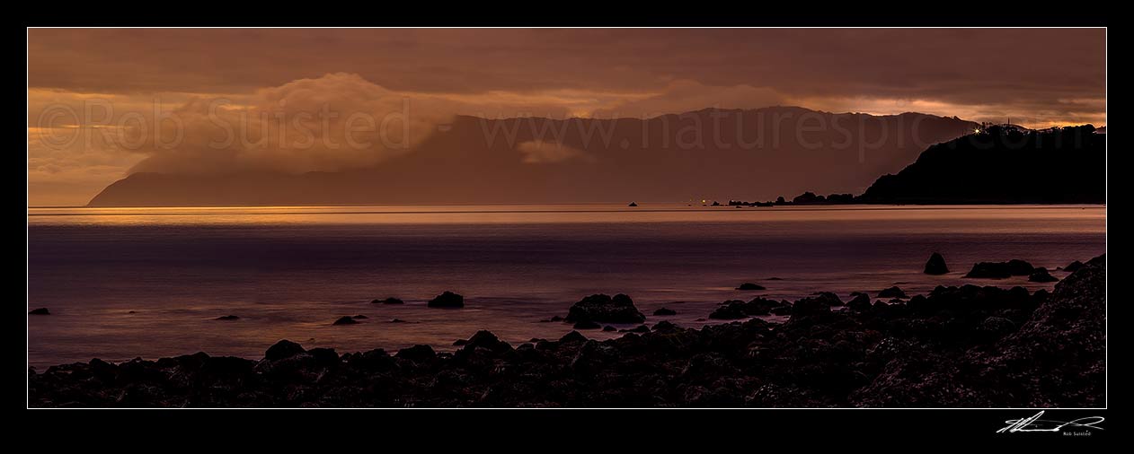 Image of Baring Head lighthouse (right) shining out over Cook Strait from Wellington harbour entrance at twilight. Sinclair Head on Wellington South Coast at left, Turakirae Head, Hutt City District, Wellington Region, New Zealand (NZ) stock photo image