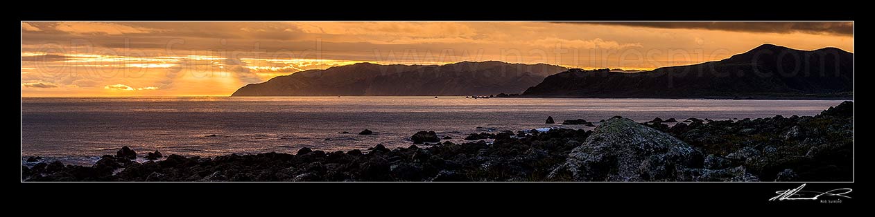 Image of Wellington South Coast at sunset. Crepuscular rays over Sinclair Head, and Baring Head at right. Seen from Turakirae Head Scientific Reserve. Panorama, Turakirae Head, Hutt City District, Wellington Region, New Zealand (NZ) stock photo image