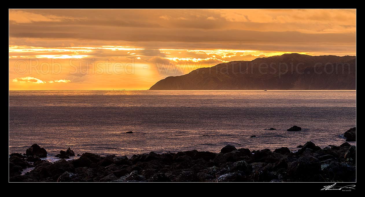 Image of Sinclair Head on Wellington South Coast, with crepuscular rays at sunset over Karori Rock lighthouse. Cook Strait at left. Seen from Turakirae Head. Panorama, Turakirae Head, Hutt City District, Wellington Region, New Zealand (NZ) stock photo image