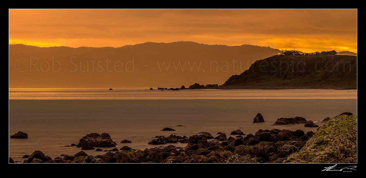 Image of Baring Head lighthouse (right) shining out over Cook Strait from Wellington harbour entrance at twilight. Sinclair Head on Wellington South Coast at left. Panorama, Turakirae Head, Hutt City District, Wellington Region, New Zealand (NZ) stock photo image