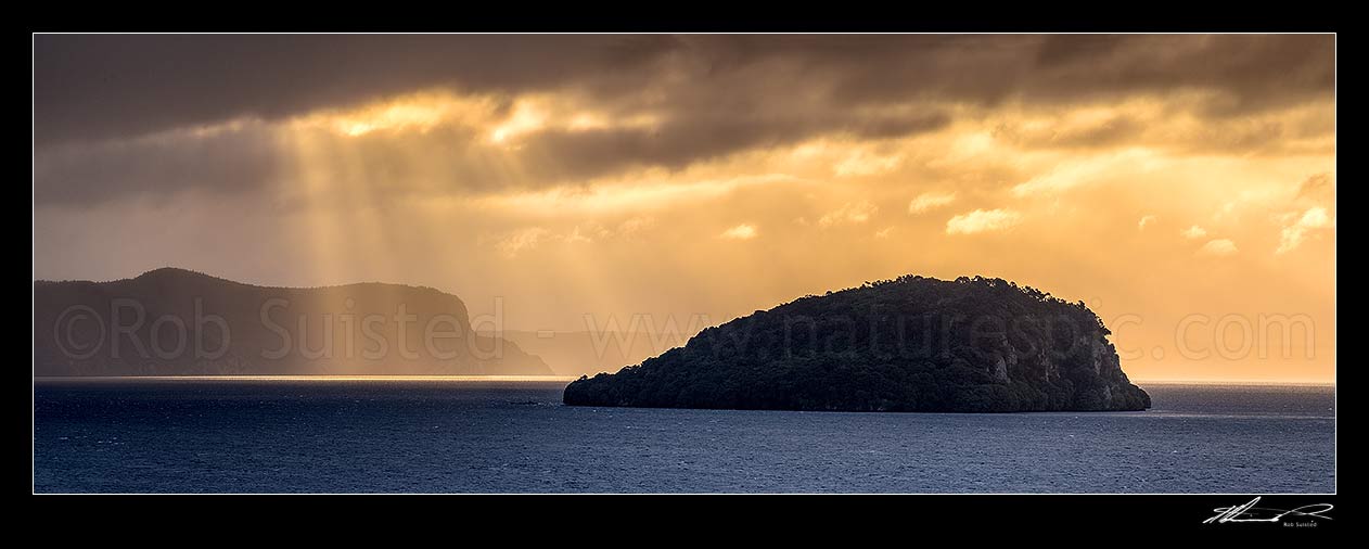 Image of Lake Taupo with moody weather breaking. Motutaiko Island in Lake Taupo (Taupomoana). Crepuscular rays on the western lake shore cliffs of Karangahape behind. Panorama, Motutere, Taupo District, Waikato Region, New Zealand (NZ) stock photo image