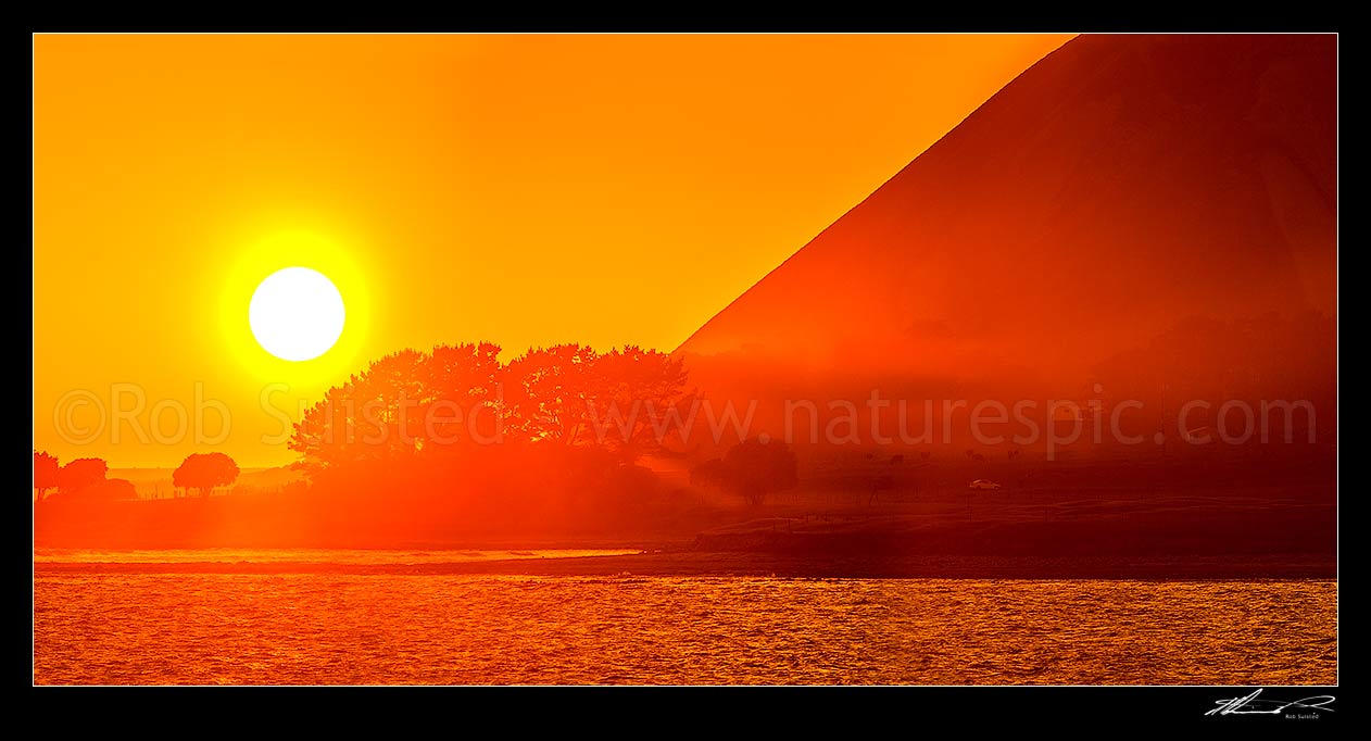 Image of Mahia Peninsula coastal sunrise at Kahutara Point (Table Cape), with sun rays through trees and morning sea mist. Panorama, Mahia, Wairoa District, Hawke's Bay Region, New Zealand (NZ) stock photo image